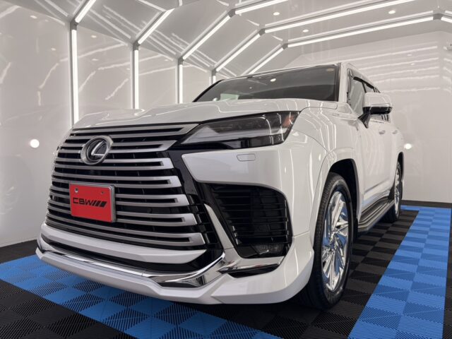 White luxury SUV in a bright showroom, front grille and headlight in focus, chrome accents visible.