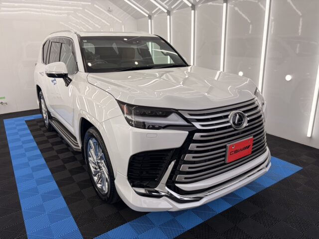 Front three-quarter view of a white luxury SUV in a bright showroom with a bold multi-bar grille and chrome accents.