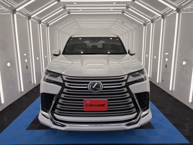 Front view of a white Lexus SUV in a bright, white-lit showroom with a prominent chrome grille and Lexus emblem at the center.