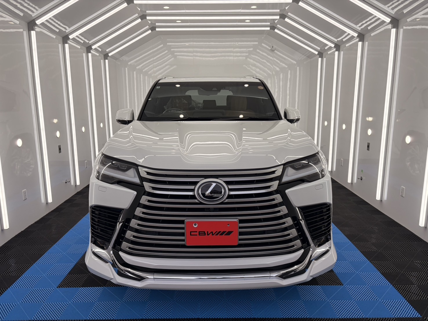 Front view of a white Lexus SUV in a bright, white-lit showroom with a prominent chrome grille and Lexus emblem at the center.