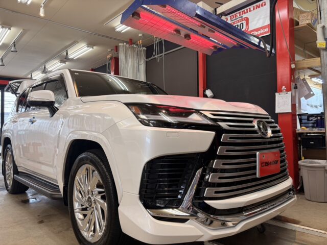 White luxury SUV on a service lift in an auto detailing shop, with a red infrared heater overhead.