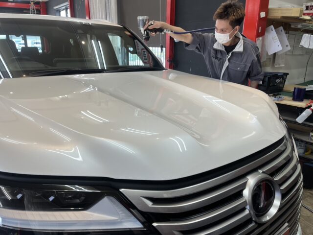 Auto detailer wearing a mask polishes the hood of a white SUV in a shop, using a handheld polisher.