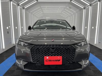 Front view of a gray SUV with a bold diamond-pattern grille in a bright white showroom with vertical LED accents on the walls.