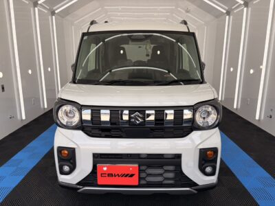 Front view of a white Suzuki compact SUV facing the camera in a bright showroom with a blue-and-black checkered floor.