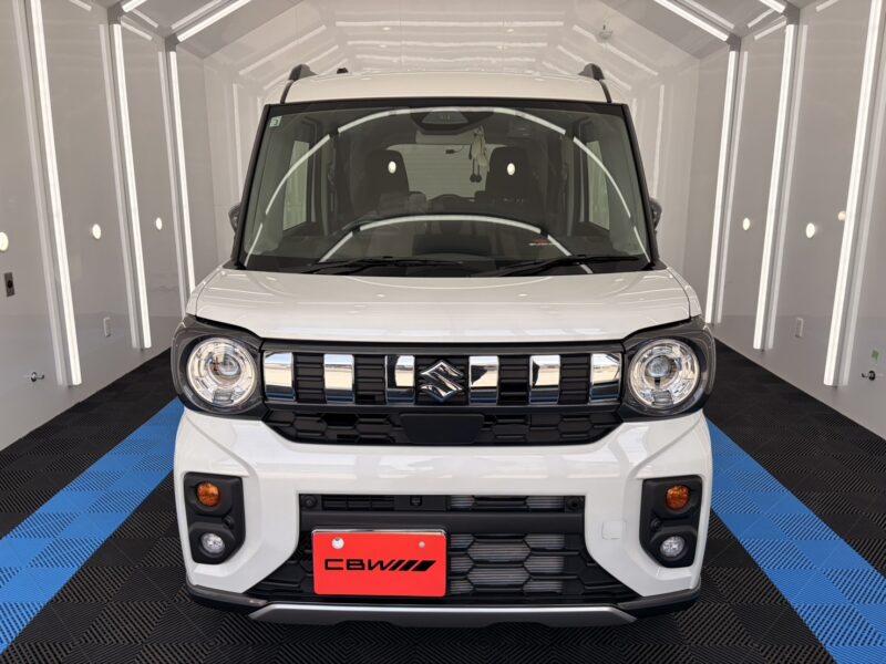 Front view of a white Suzuki compact SUV facing the camera in a bright showroom with a blue-and-black checkered floor.