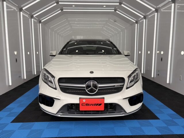 Front view of a white Mercedes‑Benz SUV facing the camera, inside a bright white studio with vertical LED accents and a blue-and-black checkered floor.