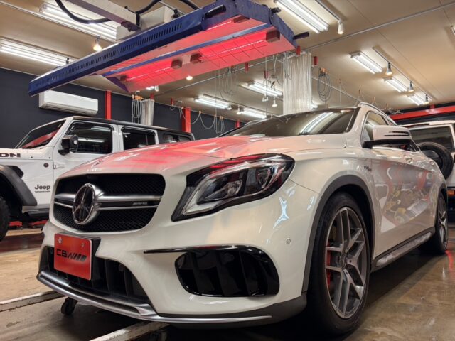 White Mercedes-Benz AMG in a car workshop, with another white SUV (Jeep) nearby and red infrared heater above.