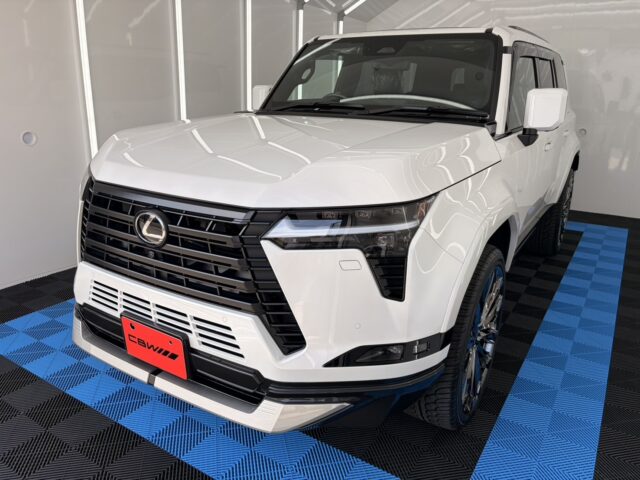 Front three-quarters view of a white Lexus SUV in a bright showroom with a blue-and-black checkered floor.