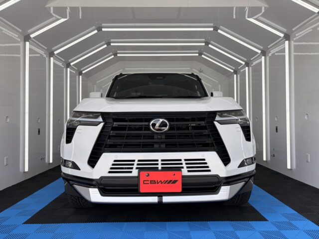 Front view of a white Lexus SUV in a bright, futuristic showroom with blue and black checkered flooring.