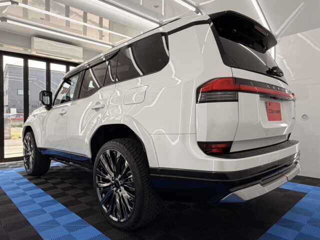 Rear-left view of a white Lexus SUV in a showroom with blue-and-black checkered floor and large chrome wheels