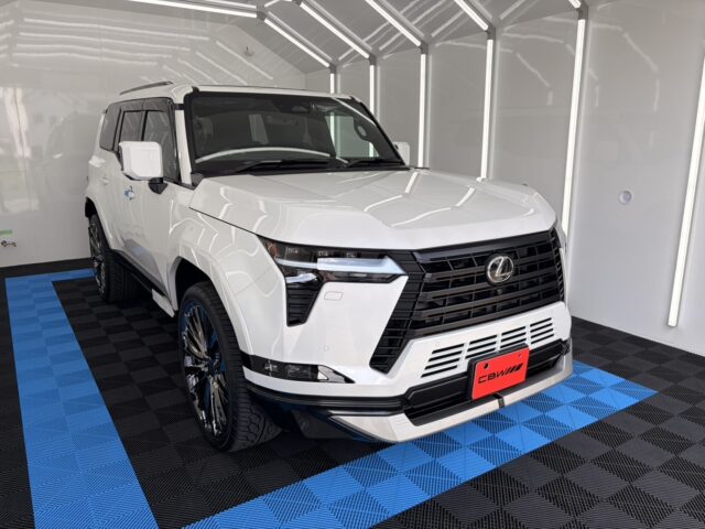 White Lexus SUV shown in a bright showroom, front three-quarter view highlighting the black grille and LED headlights, on a blue-and-black tiled floor.