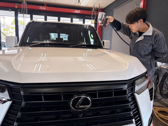 Technician in a gray jumpsuit sprays a white SUV with a paint gun inside a workshop.