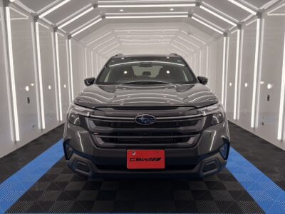 Front view of a gray Subaru SUV inside a bright, white-lit vehicle detailing booth with neon edges and a blue-and-black checkered floor, red plate at center.