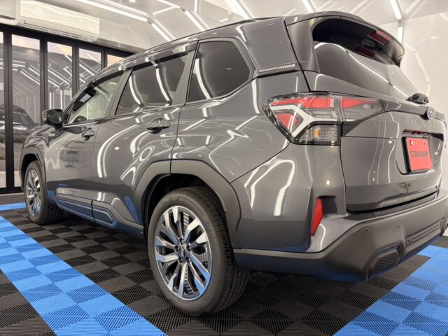 Gray Subaru Forester seen from a rear three-quarter angle inside a showroom on a blue-and-black checkered floor.