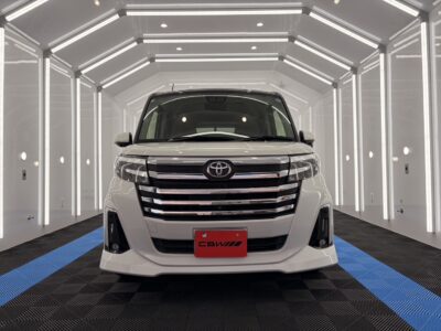 Front view of a white Toyota van in a bright, white showroom with illuminated walls and blue-striped floorplate behind it