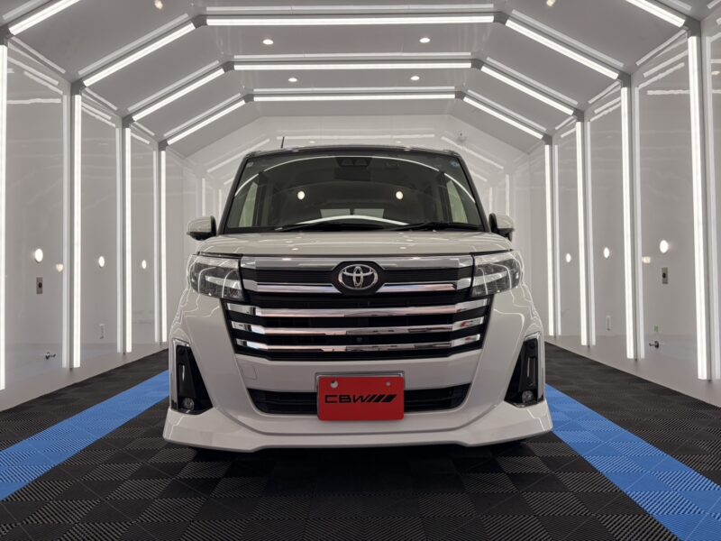 Front view of a white Toyota van in a bright, white showroom with illuminated walls and blue-striped floorplate behind it