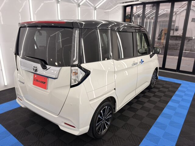 White Toyota minivan on display in a bright showroom, rear three-quarter view with tinted windows and black roof gloss.