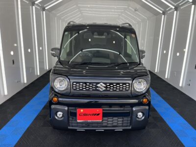 Front-on view of a dark Suzuki SUV in a bright showroom with blue-and-black checkered flooring and white walls.