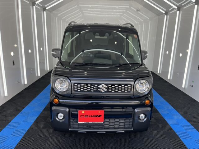 Front-on view of a dark Suzuki SUV in a bright showroom with blue-and-black checkered flooring and white walls.