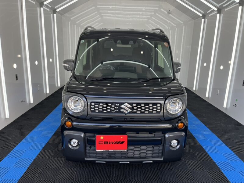 Front-on view of a dark Suzuki SUV in a bright showroom with blue-and-black checkered flooring and white walls.