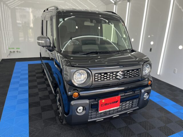 Front three-quarter view of a black Suzuki SUV in a showroom with blue-and-black checkered flooring in the background.