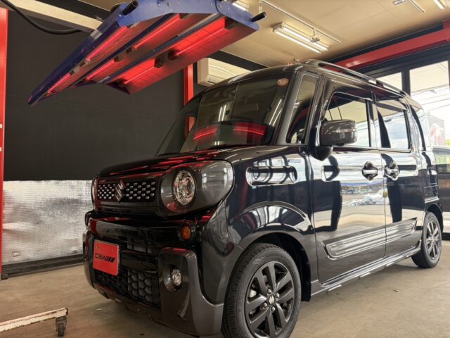 Dark gray Suzuki van in a workshop with a red overhead heater, front grille and headlights visible.