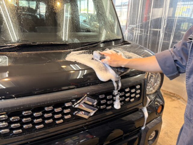 Person washing a black SUV, wiping foamy soap across the hood with a cloth.