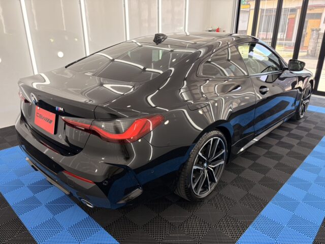 Rear three-quarter view of a dark gray BMW coupe in a showroom with blue-and-black checkered flooring.