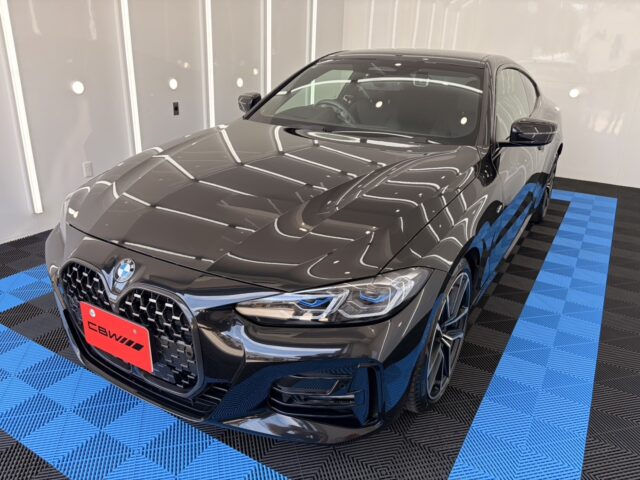 Front three-quarter view of a glossy black BMW sedan in a showroom on a blue-and-black checkered floor.