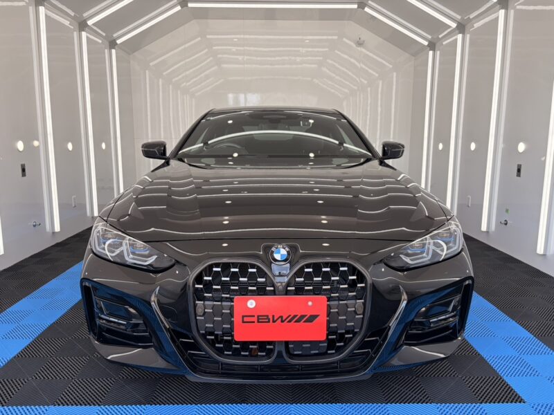 Front view of a dark gray BMW sedan in a bright showroom with a black honeycomb grille and a red license plate area visible on the bumper.