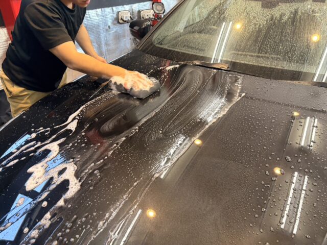 Person washing a black car hood with a soapy sponge