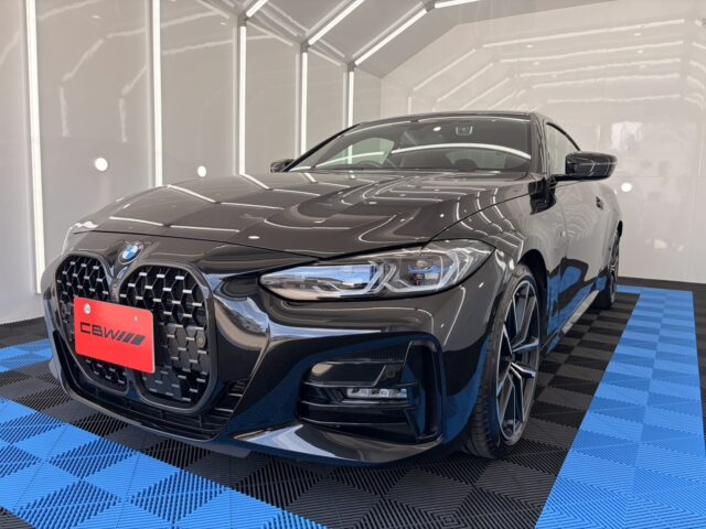 Front three-quarter view of a glossy black BMW sedan in a bright showroom with blue-and-black checkered flooring and minimal decor.