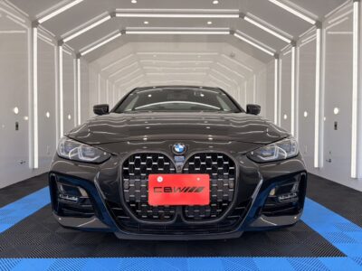 Front view of a black BMW with a large kidney grille in a bright white showroom; red EBW plate adorns the bumper.