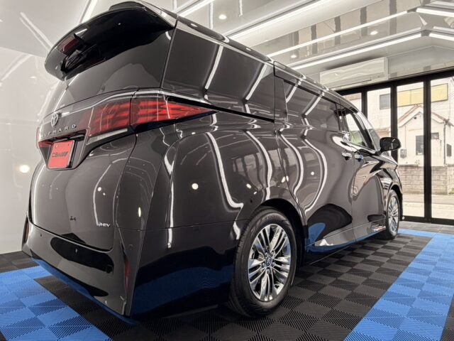 Rear three-quarter view of a black Toyota Alphard minivan in a showroom with a glossy finish and reflections on the bodywork.