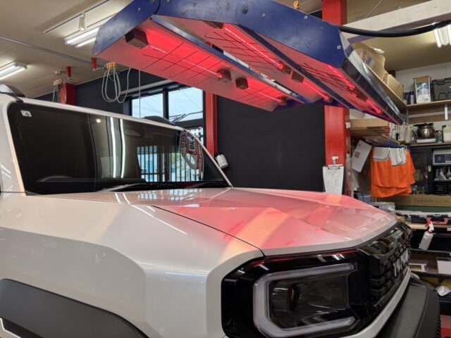 White pickup truck in a workshop, with a red infrared heater overhead.