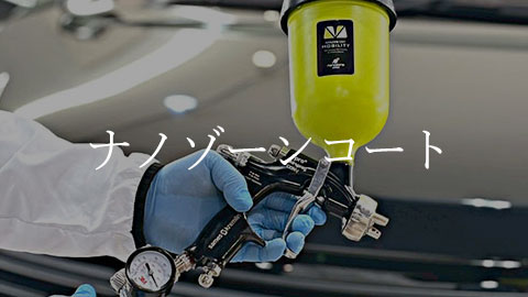 Technician wearing blue gloves holds a coating applicator connected to hoses over a dark car, with a yellow container in the background, implying a nano coating process.